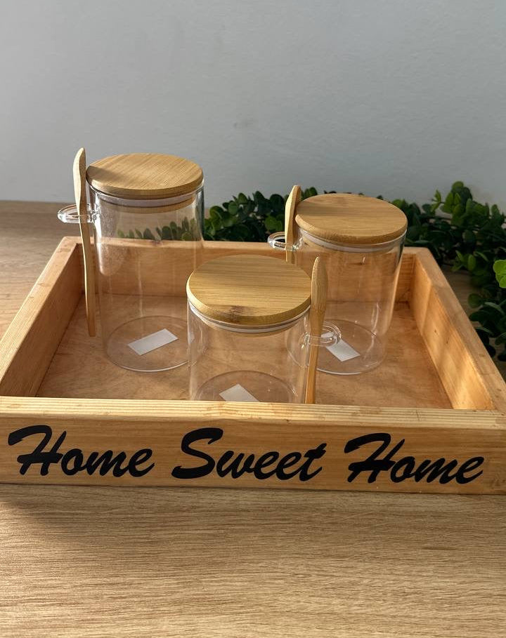 Clear jars with bamboo lids on a wooden tray with 'Home Sweet Home' engraving.