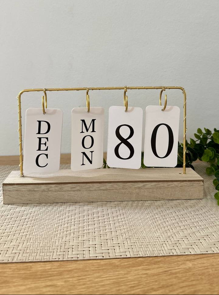 Decorative calendar with 'Dec', 'Mon', '80' on a wooden stand against a light gray background.